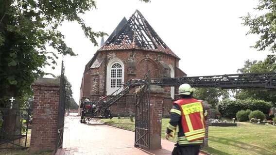 Feuerwehrmänner befinden sich vor einer abgebrannten Kirche.  
