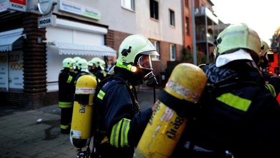 Feuerwehrleute mit Sauerstoffflaschen auf dem Rücken stehen auf einer Straße. © dpa-Bildfunk Foto: Julian Stratenschulte