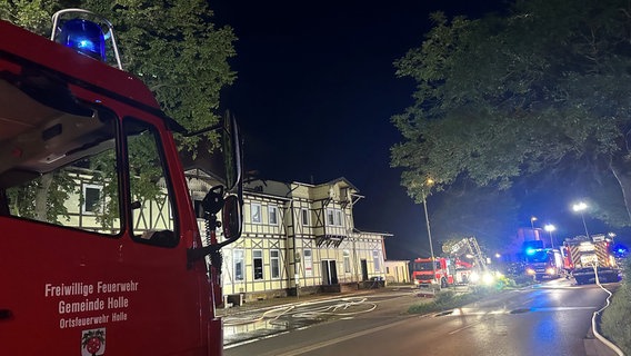 Ein rotes Feuerwehrauto steht auf einer Straße. Es ist dunkel und am Ende der Straße stehen weitere Fahrzeuge mit Blaulicht. © Polizei Hildesheim 