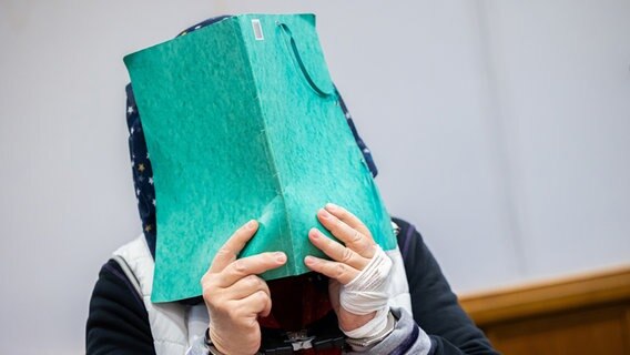 Die Angeklagte (l) steht vor Prozessbeginn in einem Gerichtssaal im Landgericht Bückeburg neben ihrem Anwalt Thilo Schäck (r) und hält sich eine Dokumentenmappe vor ihr Gesicht. © dpa-Bildfunk Foto: Michael Matthey