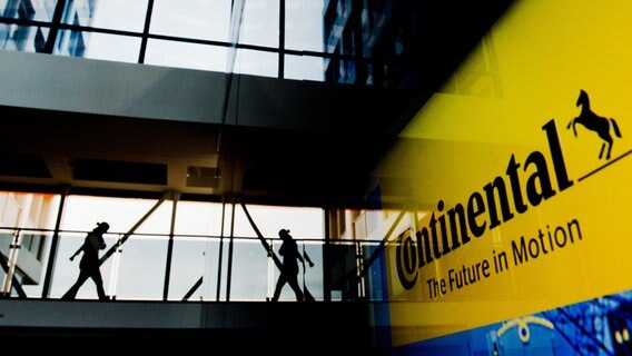 Mitarbeiter bei Continental laufen im neuen Werk in Hannover vor dem Kamera. Rechts ist ein großes Continental Schild zu sehen. © dpa Bildfunk Foto: Julian Stratenschulte