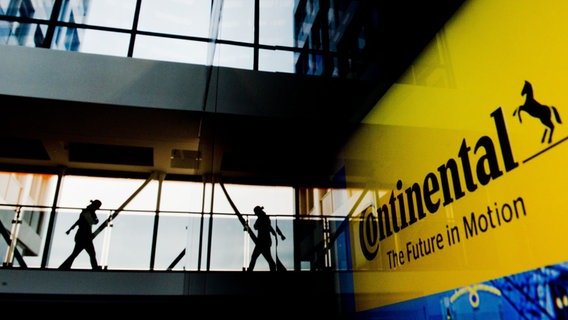 Continental-Mitarbeiter gehen durch das Continental-Werk, im Vordergrund ist das Continental-Logo zu sehen. © picture alliance/dpa Foto: Julian Stratenschulte