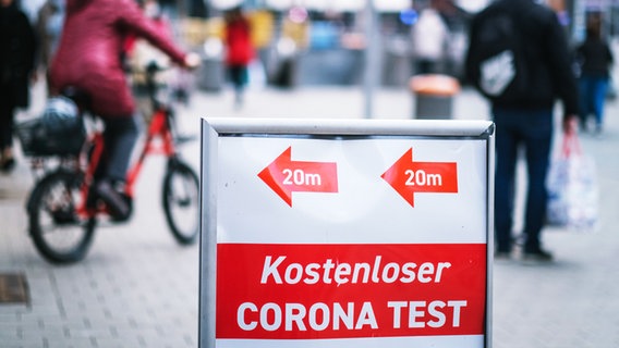 Passanten gehen in der Innenstadt an einem Schild vorbei, das auf eine Corona- Teststation und kostenlose Corona-Tests hinweist. © dpa Foto: Ole Spata