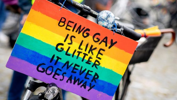 Ein Schild mit der Aufschrift «Being gay is like glitter - it never goes away» hängt im Rahmen des CSD (Christopher Street Day) am Fahrrad einer Teilnehmerin auf dem Schützenplatz in Hannover. © picture alliance/dpa | Hauke-Christian Dittrich Foto:  Hauke-Christian Dittrich