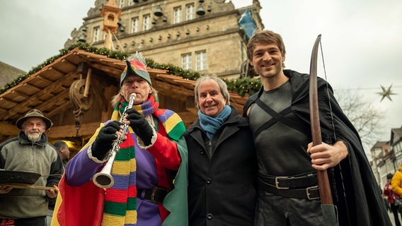Sänger Chris de Burgh steht zusammen mit einem Rattenfänger-Darsteller und einem Robin Hood-Darsteller auf dem Weihnachtsmarkt in Hameln. © Hameln Marketing und Tourismus GmbH 