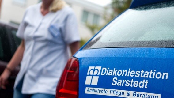 Eine Mitarbeiterin eines Pflegedienstes geht an ihrem geparkten Dienstwagen vorbei. © picture alliance / dpa | Sebastian Gollnow Foto: Sebastian Gollnow