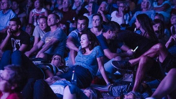 Besucher des NDR Klassik Open Air 2018 (Generalprobe) sitzen in lila Licht auf dem Boden. © NDR Foto: Julius Matuschik