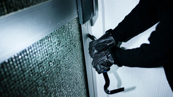 Eine Person mit schwarzen Lederhandschuhen versucht mit einem Brecheisen eine Haustür aufzubrechen. © NDR Foto: Julius Matuschik