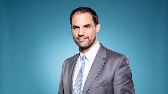 Christopher Emden steht vor einem blauen Hintergrund im Porträt. © Christopher Emden 