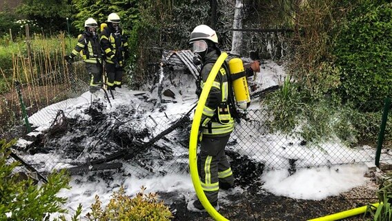 Feuerwehrleute stehen an einer neidergebrannten Gartenhütte. © Polizeiinspektion Hameln-Pyrmont/Holzminden 
