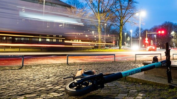 Ein E-Scooter liegt in der Morgendämmerung auf einem Gehweg in der Innenstadt, während auf der Straße LKW vorbeifahren. © dpa-Bildfunk Foto: David Hutzler