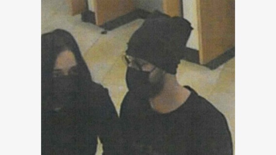 Eine Frau und ein Mann haben ihr Gesicht mit schwarzen Masken bedeckt und stehen in einer Bank. Die Aufnahme stammt von einer Überwachungskamera. © Polizei Hannover 