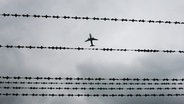 Ein Flugzeug fliegt am Flughafen in Hannover über Stacheldraht. © dpa-Bildfunk Foto: Julian Stratenschulte
