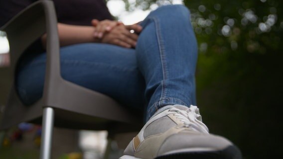 Das Bild zeigt die Beine einer Frau, die auf einem Stuhl sitzt. © NDR 
