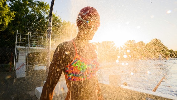 Hannover: Eine Frühschwimmerin steht im Licht der aufgehenden Sonne im Freibad Annabad unter einer Dusche. © dpa-Bildfunk Foto: Julian Stratenschulte