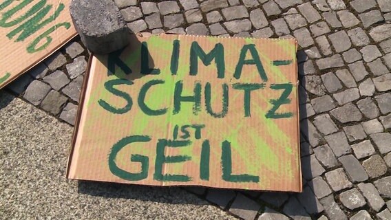 Ein Protestplakat aus Pappe liegt auf dem Boden, darauf steht "Klimaschutz ist geil".  