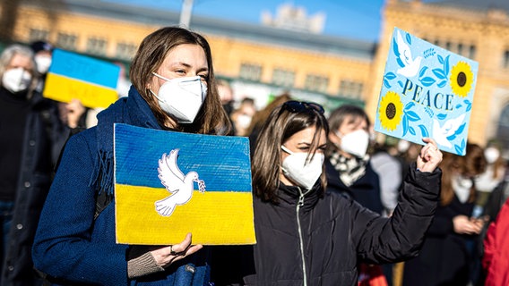 Eine Friedenstaube ist auf dem Plakat einer Demonstrantin auf einer Demonstration gegen den Angriff Russlands auf die Ukraine zu sehen - auf einem weiteren Plakat ist der Schriftzug "peace" zu lesen. © picture alliance Foto: Moritz Frankenberg