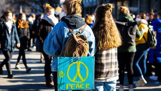 Der Schriftzug "peace" ist zusammen mit einem Friedenszeichen auf dem Plakat einer Demonstrantin auf einer Demonstration gegen den Angriff Russlands auf die Ukraine zu lesen. © dpa Foto: Moritz Frankenberg