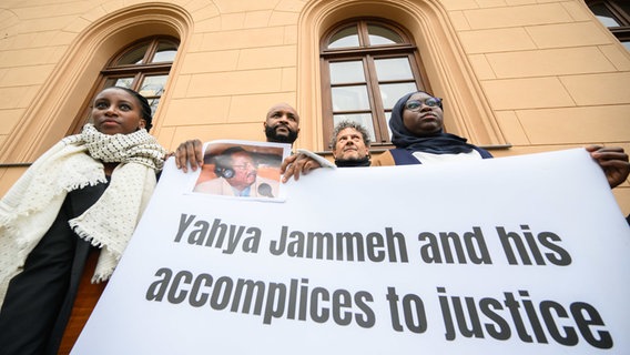 Baba Hydara, Sohn des getöteten gambischen Journalisten Deyda Hydara, steht mit einem Foto seines Vaters und mit Aktivisten vor dem Oberlandesgericht Celle. © dpa Foto: Julian Stratenschulte