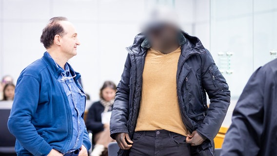 Der gambische Angeklagte (r) steht im Gerichtssaal. Wegen Verbrechen gegen die Menschlichkeit, Mordes und versuchten Mordes hat die Bundesanwaltschaft am Oberlandesgericht Celle Anklage gegen ein ehemaliges Mitglied der gambischen Streitkräfte erhoben. © Moritz Frankenberg/dpa Foto: Moritz Frankenberg