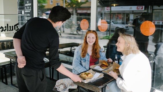 Zwei Frauen werden von einem Kellner im Außenbereich einer Fastfoodkette bedient. © dpa-Bildfunk Foto: Ole Spata