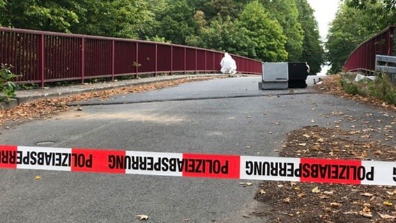 Ein Mann in weißer Schutzkleidung auf einer Autobahnbrücke der A7. Davor ein Absperrband der Polizei. © Polizeiinspektion Hildesheim Foto: Polizeiinspektion Hildesheim