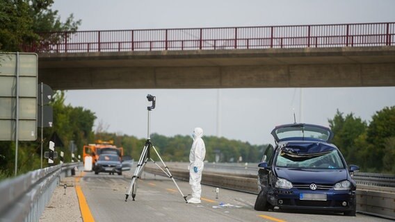 Stark beschädigtes Fahrzeug auf der Autobahn 7. Daneben eine Person in weißem Schutzanzug. © Clemens Heidrich/dpa Foto: Clemens Heidrich