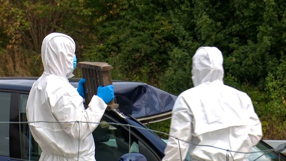 Einsatzkräfte in weißer Schutzkleidung halten den Gullydeckel in der Hand, der in das Fahrzeug einschlug. © Hannover Reporter Foto: Hannover Reporter