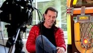 Der Musiker Albert Hammond sitzt neben einer Jukebox im NDR1 Studio. Eine Kamera steht im Vordergrund. © NDR Foto: Henning Martin