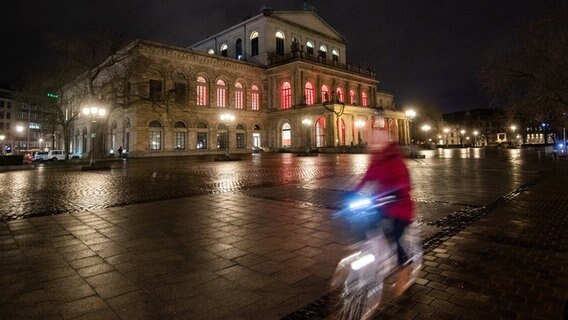 Eine Radfahrerin (mit Bewegungsunschärfe) auf einem Fahrradweg vor der Oper Hannover. Die Fenster der Oper leuchten rot. © dpa-Bildfunk Foto: Julian Stratenschulte