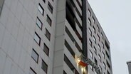 Ein Feuerwehrmann fährt mit einem Kran zu einer ausgebrannten Wohnung in einem Hochhaus in Hannover. © HannoverReporter 