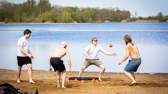 Eine Gruppe junger Männer spielt bei sonnigem Wetter am Ufer vom Hufeisensee in der Region Hannover "Spikeball". © dpa-Bildfunk Foto: Moritz Frankenberg