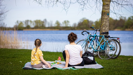 Isernhagen: Eine Frau und ein Kind sitzen bei sonnigem Wetter am Ufer vom Hufeisensee in der Region Hannover. © dpa-Bildfunk Foto: Moritz Frankenberg