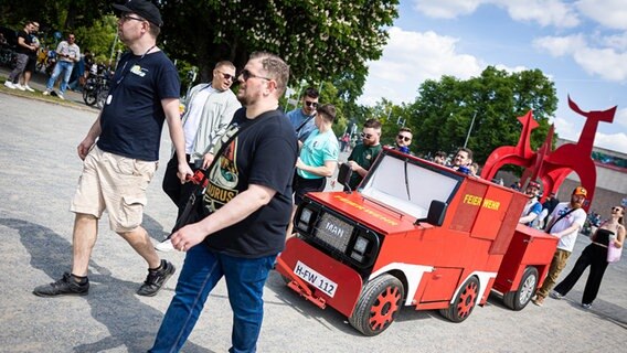 Männer ziehen am Vatertag am Maschsee-Nordufer einen Bollerwagen mit der Aufschrift "Feierwehr". © dpa Foto: Moritz Frankenberg