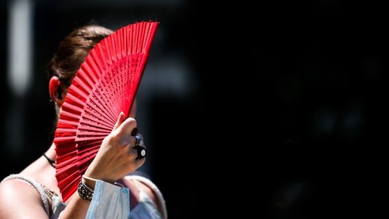 Eine Frau fächert sich Luft zu mit einem roten Fächer. © Julian Stratenschulte/dpa Foto: Julian Stratenschulte
