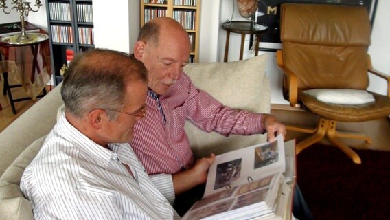 Reinhard Lüschow (vorne) und Heinz-Friedrich Harre schauen sich auf dem Sofa sitzend ein Fotoalbum an. © NDR Foto: Kathrin Riggert