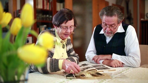 Erika Hesse und ein Mann, der zu ihrer Linken sitzt, betrachten gemeinsam ein Fotoalbum. © NDR 