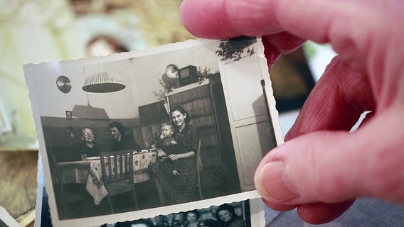 Erika Hesse hält eine alte schwarzweiß Fotografie, die sie mit ihrer Familie zeigt, in ihrer Hand. © NDR 