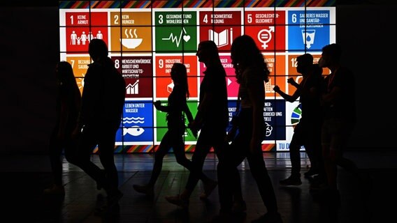 Eine Schülergruppe läuft bei IdeenExpo in der Messe Hannover am Stand von Engagement Global an einer Leinwand mit 17 Nachhaltigkeitszielen vorbei. © Julian Stratenschulte/dpa Foto: Julian Stratenschulte