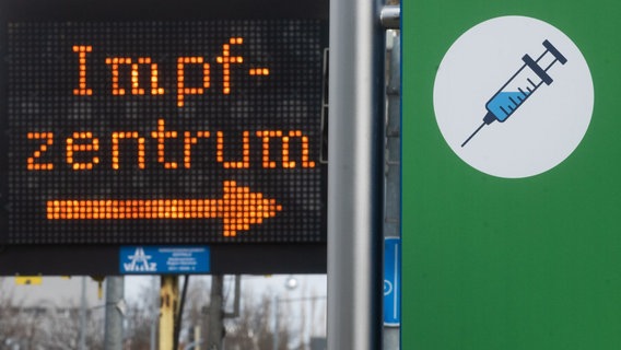 Eine elektronische Anzeigetafel mit dem Wort "Impfzentrum" und ein Plakat mit der Abbildung einer Spritze weisen den Weg zum Impfzentrum auf dem Messegelände in Hannover. © dpa-Bildfunk Foto: Julian Stratenschulte