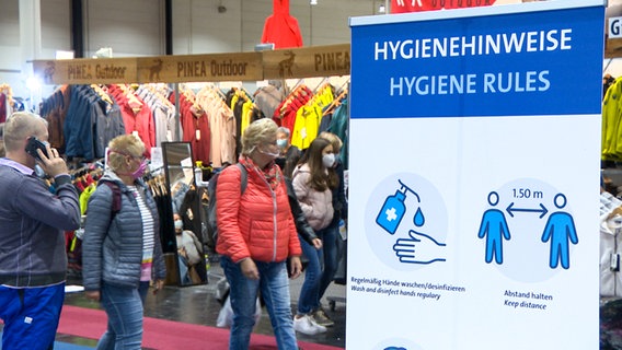 In einer Messehalle steht ein Banner mit der Aufschrift "Hygienehinweise". © NDR 