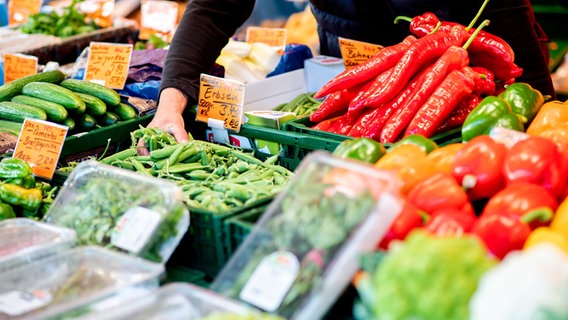 An einem Obst- und Gemüsestand greift ein Verkäufer auf dem Wochenmarkt in eine Kiste mit Erbsen. © dpa-Bildfunk Foto: Hauke-Christian Dittrich