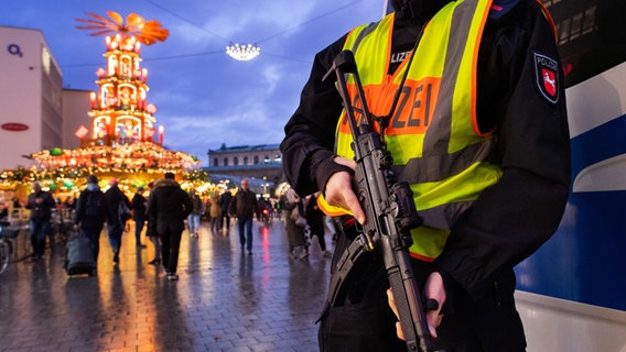 Schwer bewaffnete Polizisten mit Maschinenpistolen sichern die Weihnachtspyramide am Kröpcke unweit des Weihnachtsmarktes in der Abenddämmerung. Die nach Angaben der Stadt Hannover größte begehbare Weihnachtspyramide der Welt ist 18 Meter hoch und sorgt in der Innenstadt für weihnachtliche Stimmung. © picture alliance/dpa Foto: Julian Stratenschulte