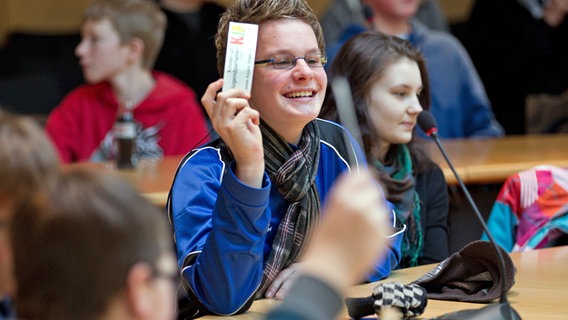 Ein Junge hält einen Zettel mit der Aufschrift "Kinder- und Jugendparlament" in die Luft. © dpa - Picture Alliance Foto: Friso Gentsch