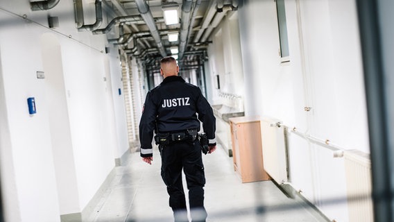 Ein Beamter des Justiz Vollzuges geht durch einen Gang in einem Gefängnistrakt. © NDR Foto: Julius Matuschik