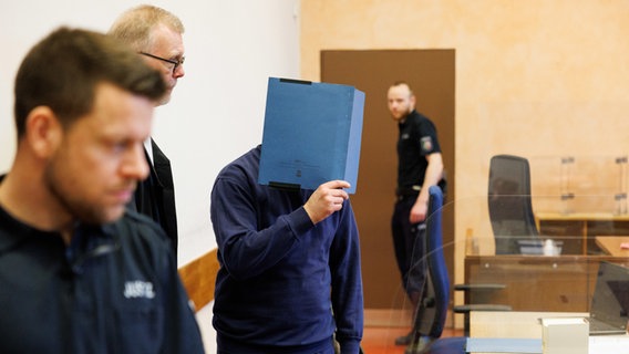 Ein Rechtsanwalt steht mit seinem Mandanten und zwei Justizmitarbeitern in einem Saal im Landgericht Detmold. © picture alliance/dpa Foto: Friso Gentsch