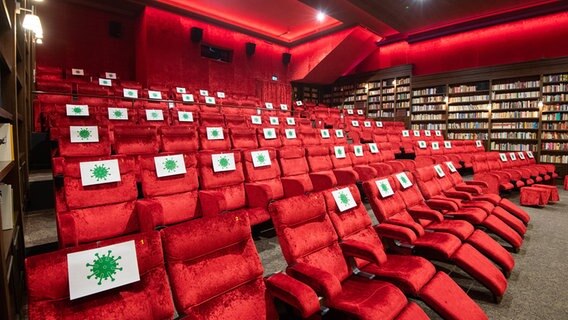 Auf mehreren Sitzen in einem Kinosaal des Kinos Astor Grand Cinema sind Zettel mit runden Figuren abgedruckt, die der Form und Struktur des Corona-Virus nachempfunden sind. © dpa - Bildfunk Foto: Julian Stratenschulte
