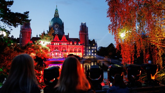 Besucher stehen am See im Maschpark und schauen sich das Konzert vor dem Neuen Rathaus auf der anderen Uferseite an. Besucher stehen am See im Maschpark und schauen sich das Konzert vor dem Neuen Rathaus auf der anderen Uferseite an. © Michael Matthey/dpa Foto: Michael Matthey
