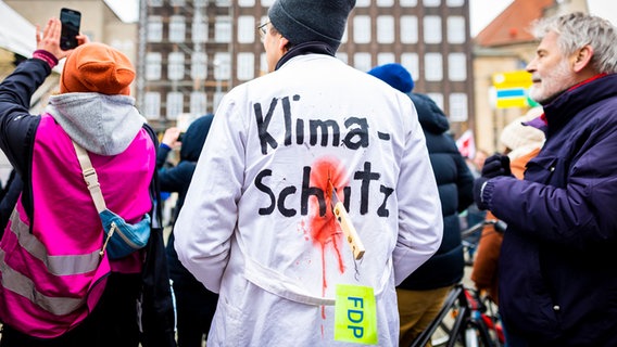 Der Schriftzug "Klima-Schutz" und ein Messer mit einem Anhänger "FDP" sind auf dem Rücken eines Demonstranten bei einer Kundgebung zu Klimastreik von Fridays for Future in Hannover zu sehen. © dpa 
