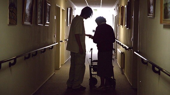 Frau mit Gehhilfe und Pfleger in einem Seniorenwohnheim. © dpa/Picture-alliance Foto: Alexander Stein